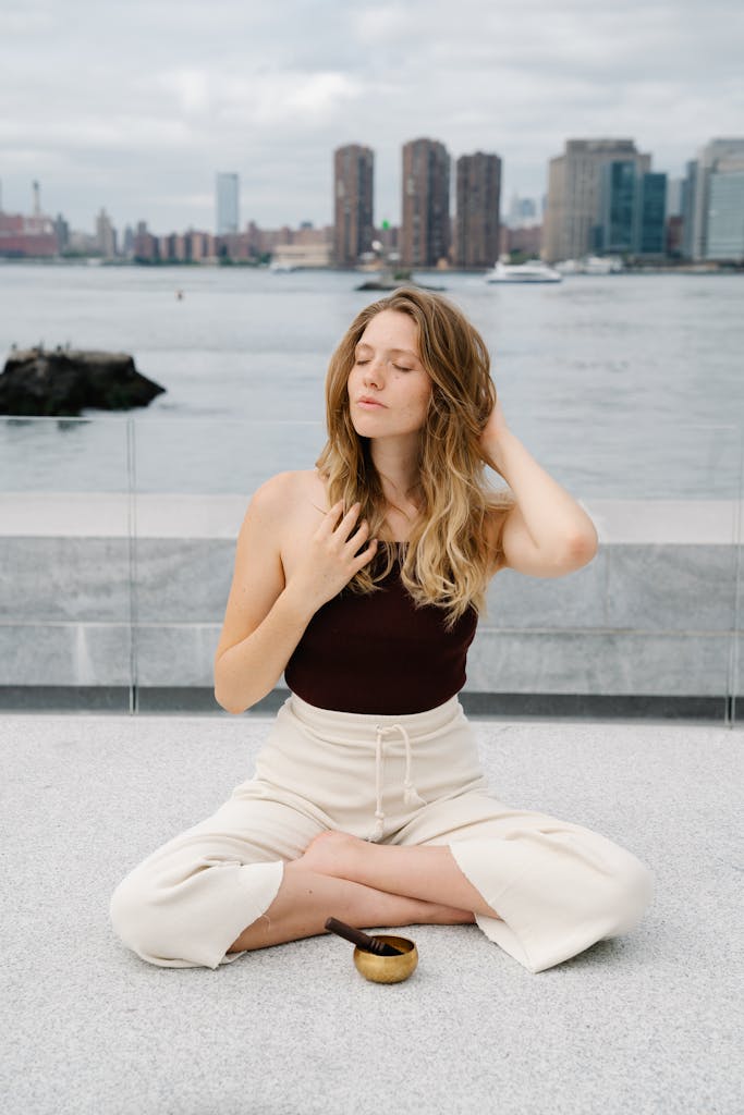 Woman practicing meditation outdoors with a cityscape view, peaceful and serene.